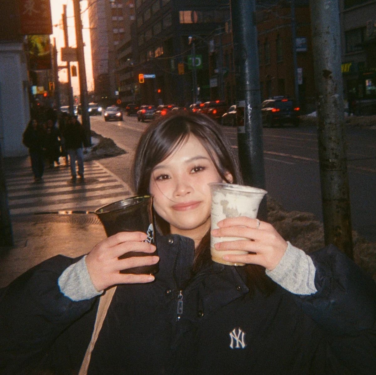 Holding up two drinks on a city street at sunset